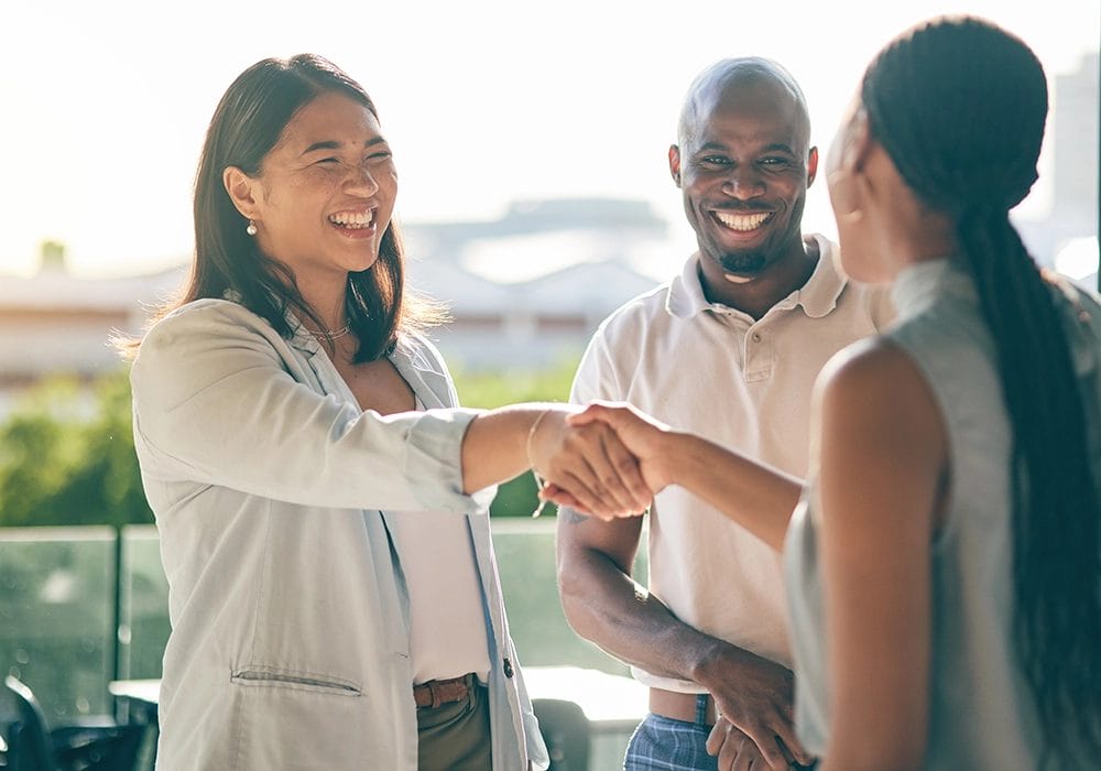 Three business people showcasing social proof as they confidently shake hands in front of a building.