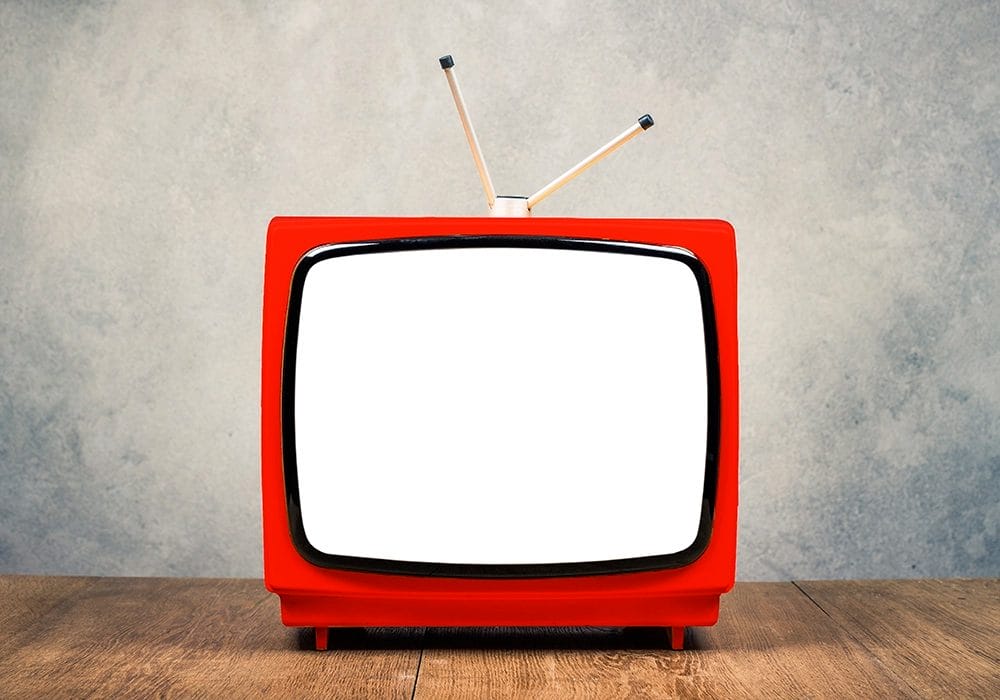 A traditional advertising medium - a red TV with a blank screen - placed on a wooden table.