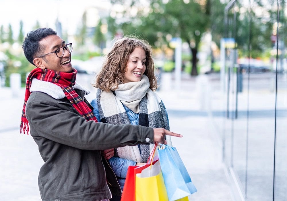 A couple making purchase decisions, holding shopping bags in front of a store.