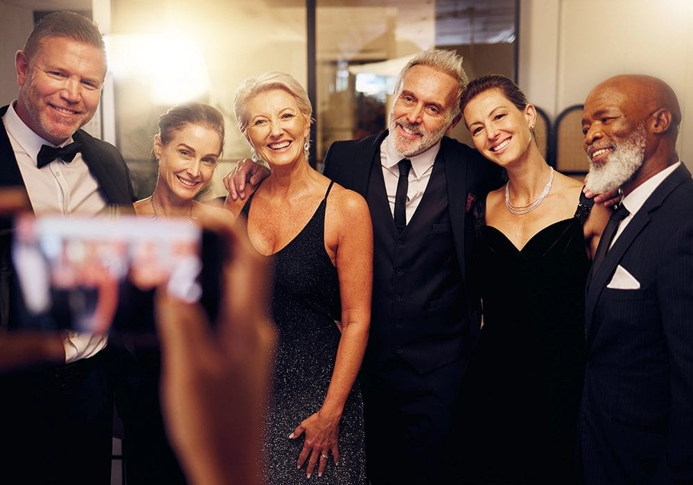 Group of elegantly dressed adults posing for a celebrity endorsement photo.