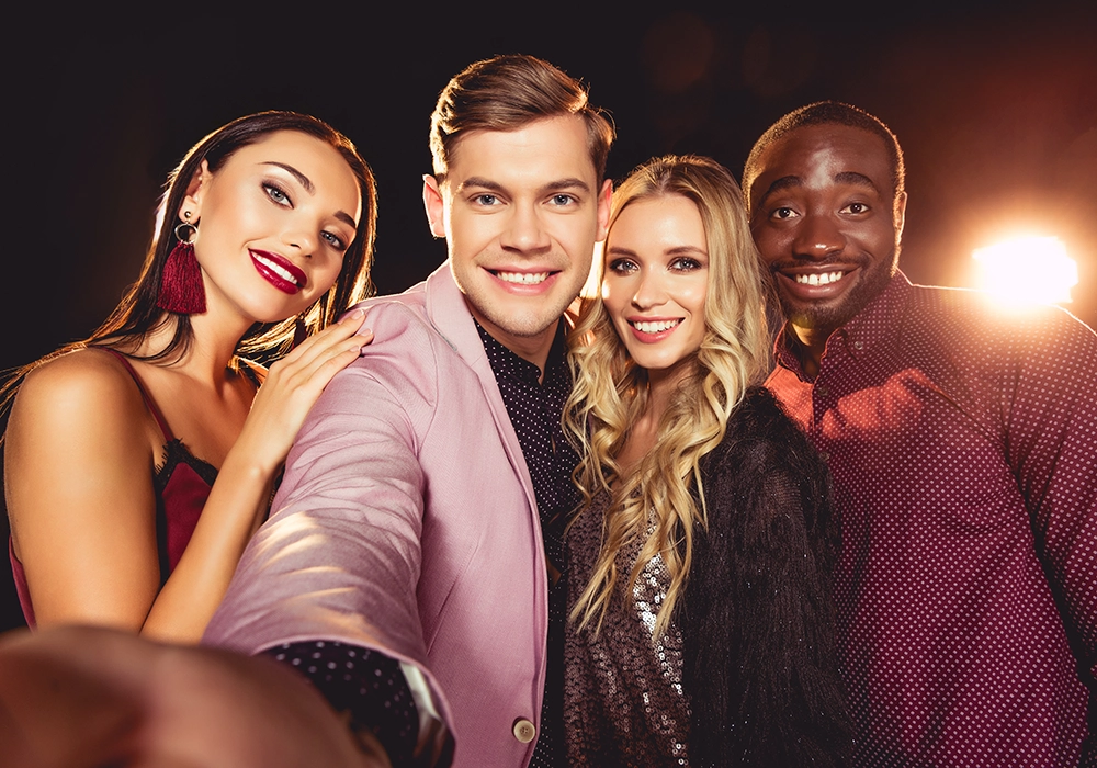 Four celebrity friends posing together for a photo with a warm backlight.