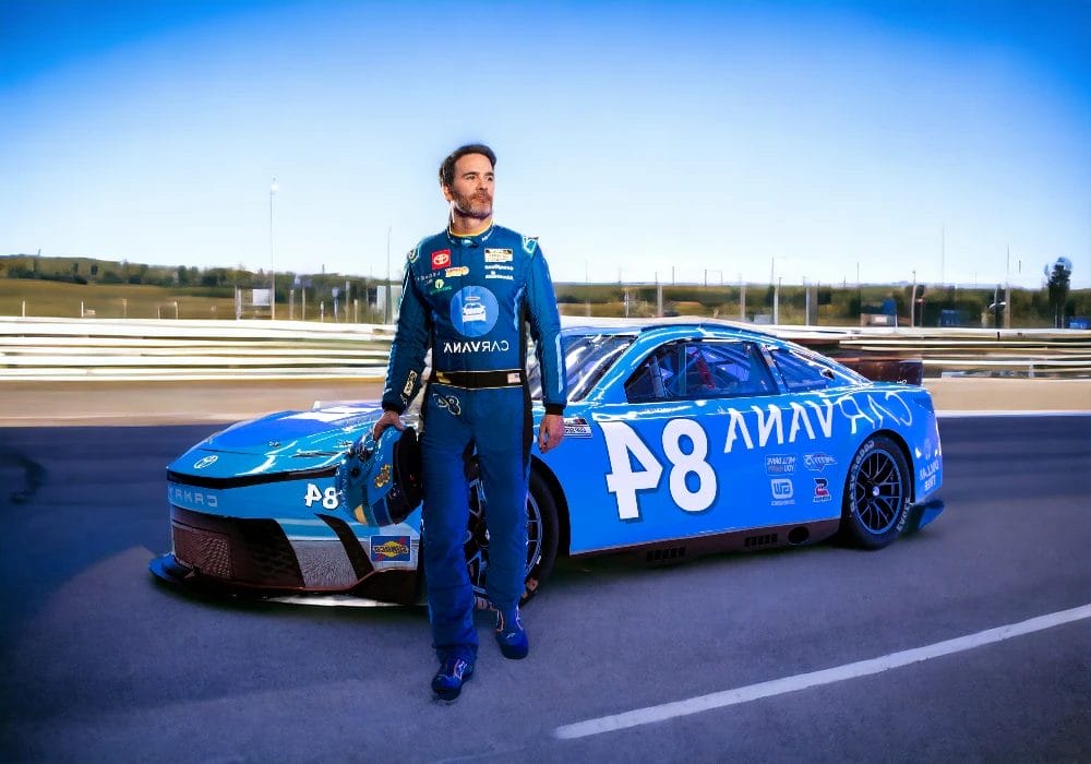 A NASCAR race car driver in a blue racing suit stands confidently next to a blue race car marked with the number 48 on a racetrack under a clear sky, showcasing celebrity endorsements.