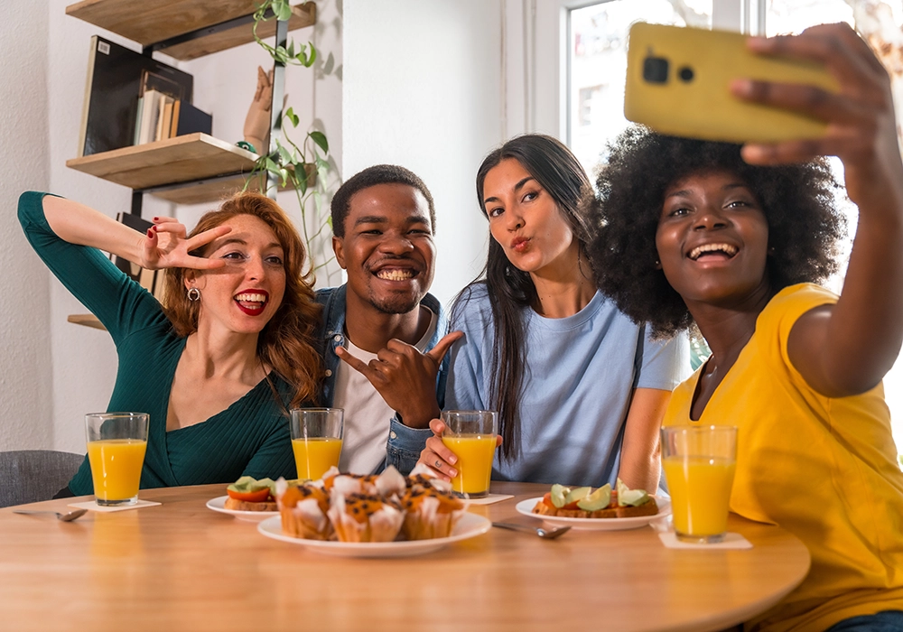 Four people sitting at a table with food and drinks, smiling and posing for a selfie—perfect for showcasing influencer marketing for startups.