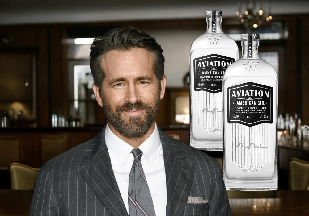 Ryan Reynolds stands in front of a bar with two bottles of Aviation American Gin displayed beside him, exemplifying the power of celebrity endorsements on beverage brands.