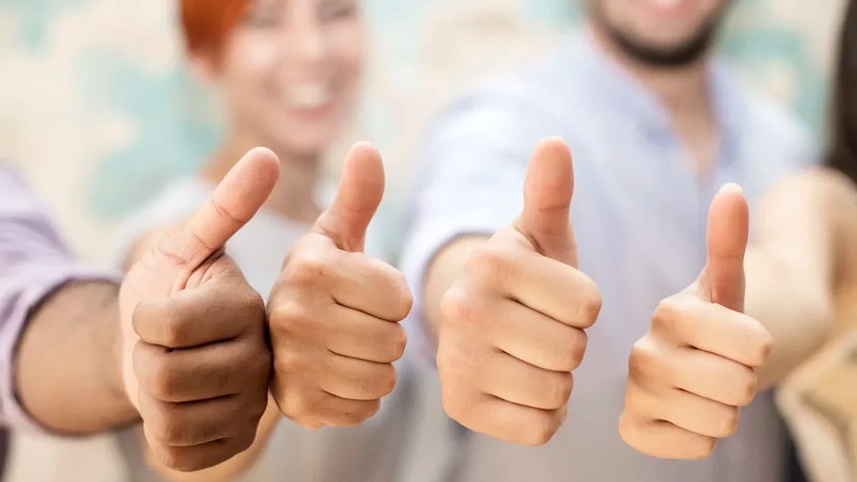 Four people standing side by side, each giving a thumbs-up gesture—a scene reminiscent of positive review response examples—with faces blurred in the background and hands in focus.