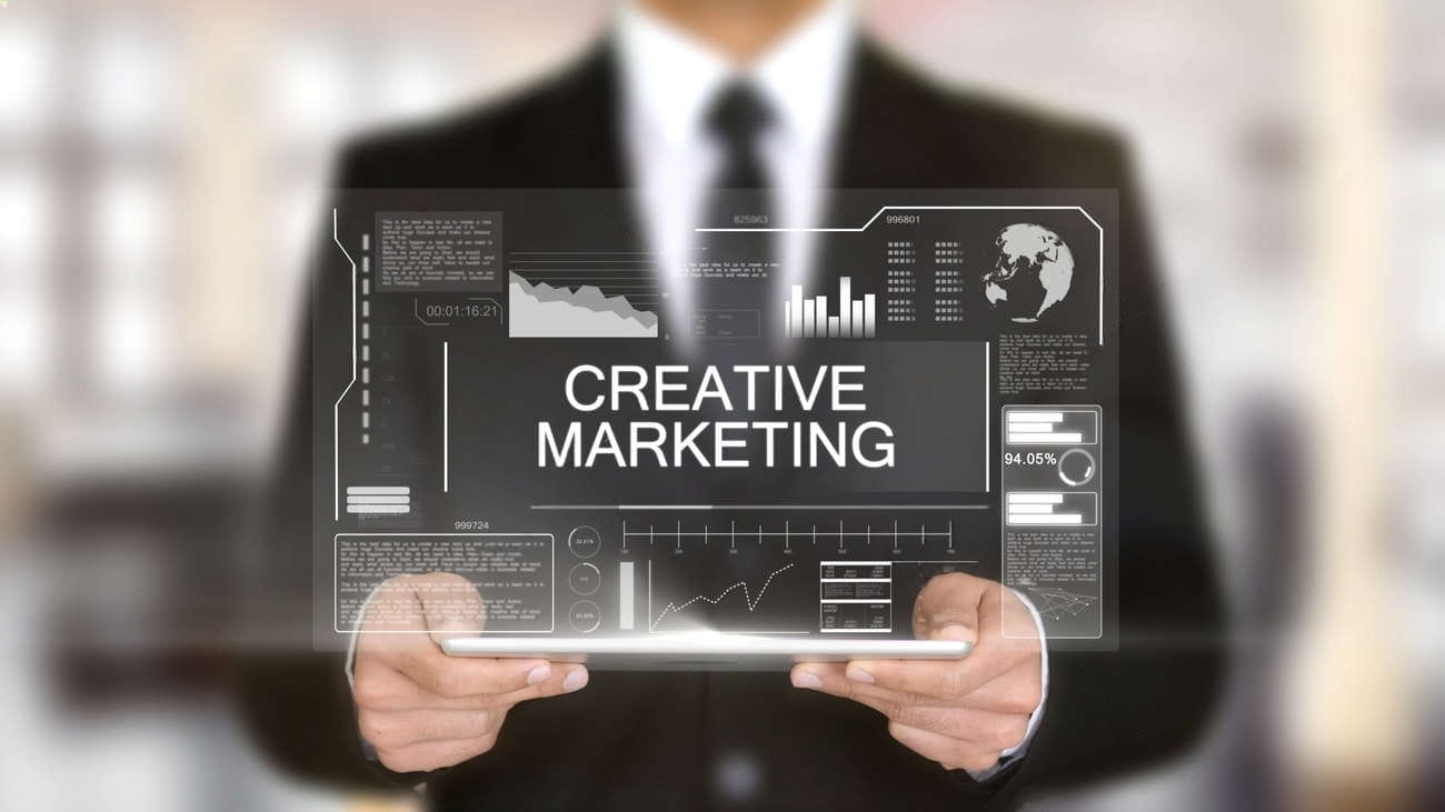 A person in a suit holds a transparent digital screen displaying the words "Creative Digital Marketing" with various charts and graphs visible in the background.